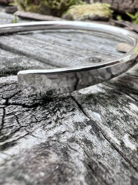 Close-up of a handmade sterling silver Aurora Crescent torque bangle showing the hammered texture and open crescent ends
