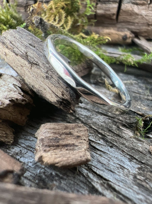 Close-up of a handmade sterling silver flat hammered ring on driftwood, highlighting the smooth hammered flat surface