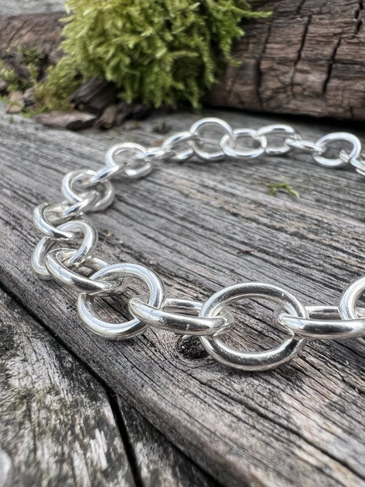 Close-up of a handmade sterling silver Lina trace bracelet on wooden surface, highlighting the chunky oval trace chain links