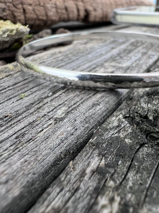 Close-up of a handmade sterling silver minimal luxe bangle on wood, highlighting the slim polished textured wire band