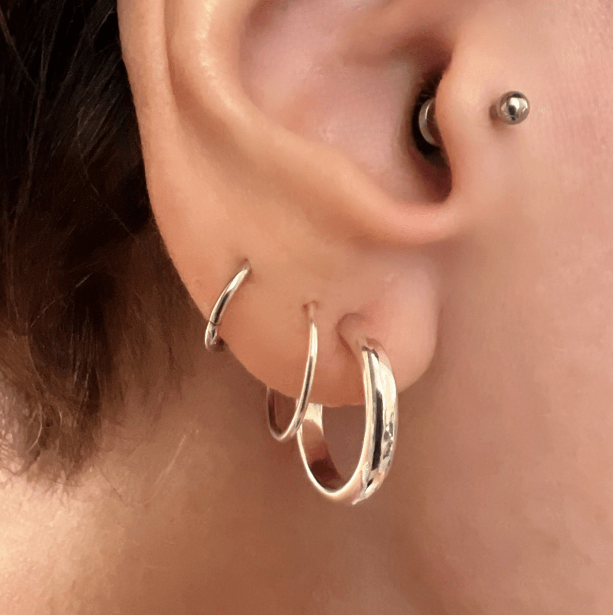 Recycled silver mini luxe hoop small earrings worn with a small stud, showing how the hoops layer for an ear stack look