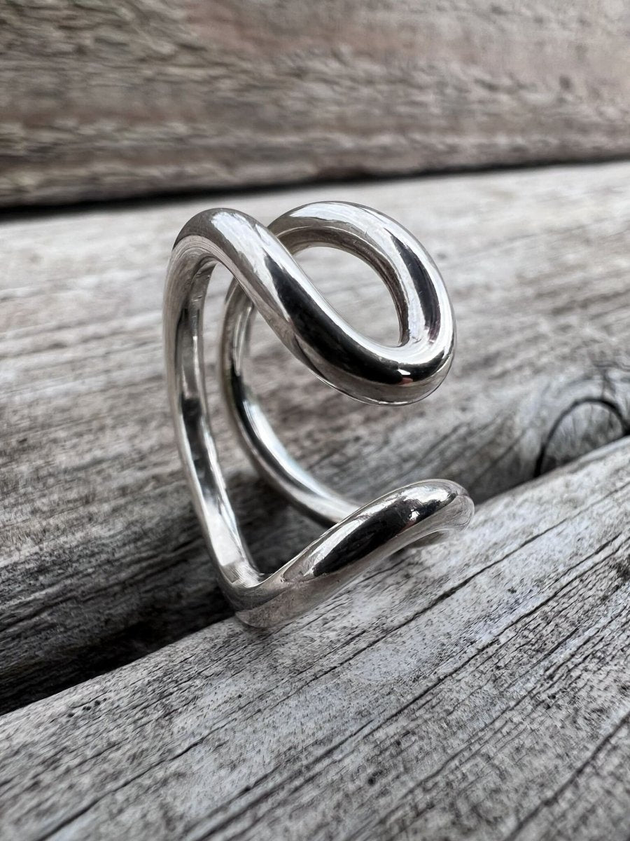 Recycled silver open loop ring photographed from a side angle on driftwood, highlighting the sculptural looped form