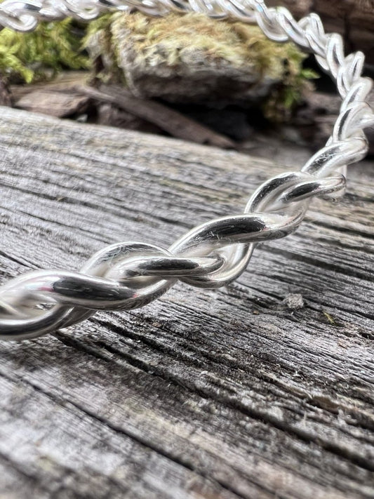 Close-up of a handmade sterling silver open twist bangle on wood, highlighting the twisted texture
