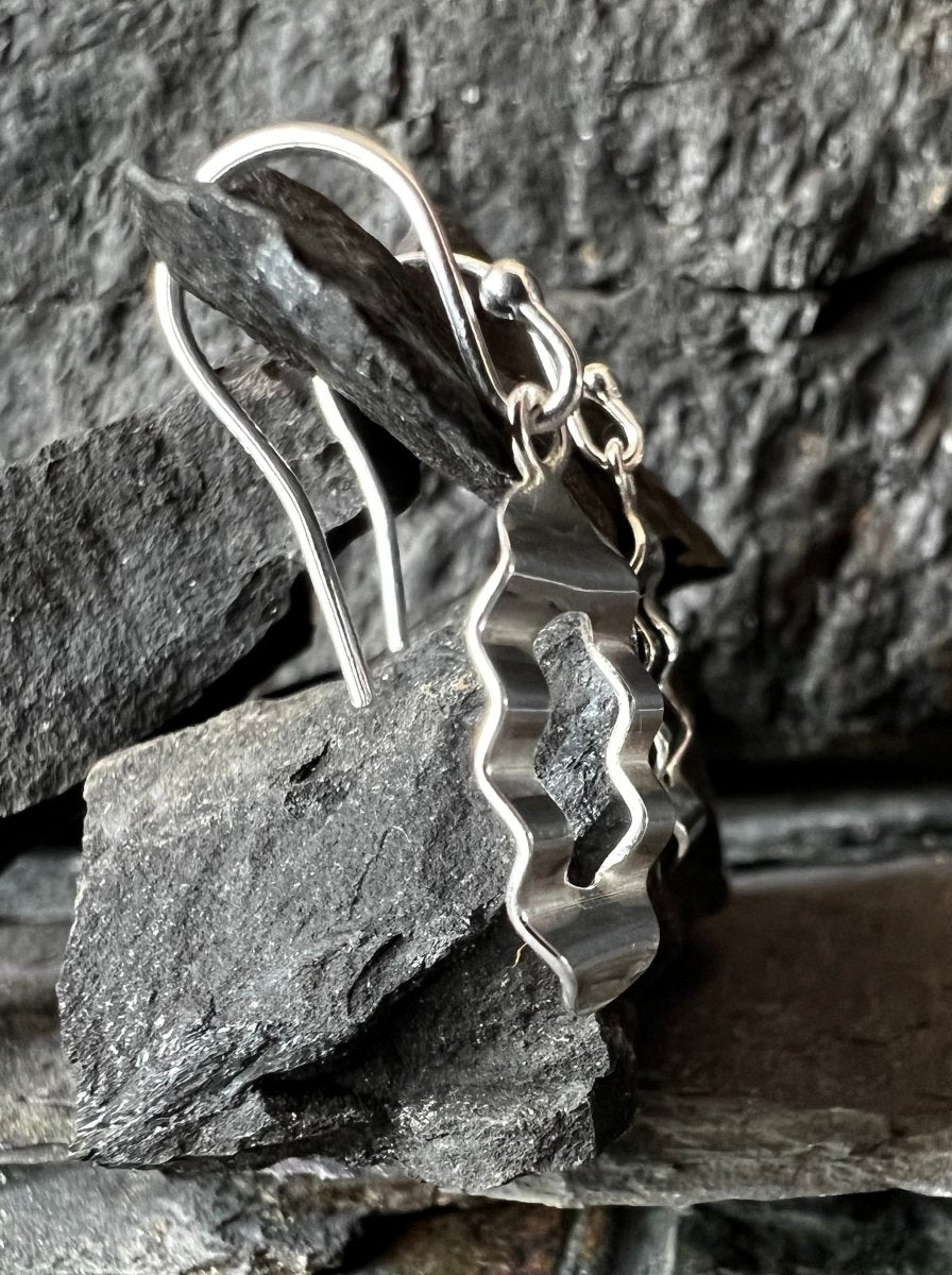Silver wavy earrings on a stone background