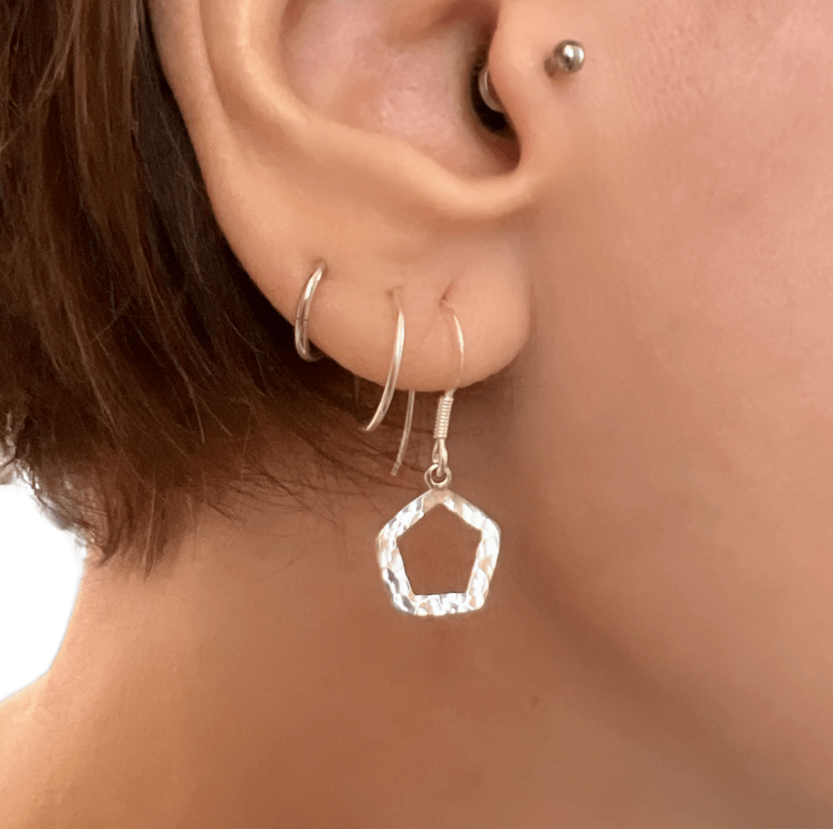 Sterling silver textured pentagon earrings worn in ear, showing the geometric open pendant and drop length against skin