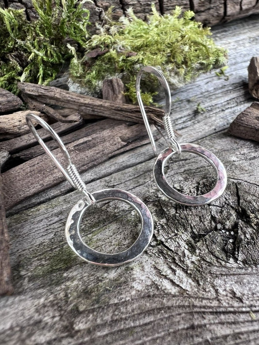 Close-up of handmade sterling silver radiant circle earrings on weathered wood, showing the open circle design and wire hook