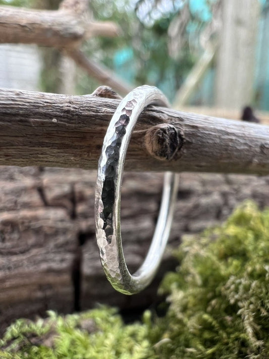 Close-up of a handmade silver stacking ring showing hammered texture detail, photographed against wood and moss