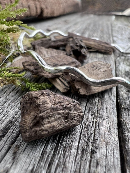Close-up of a handmade sterling silver 2.5mm wave bangle on weathered wood, highlighting the fine undulating wave texture