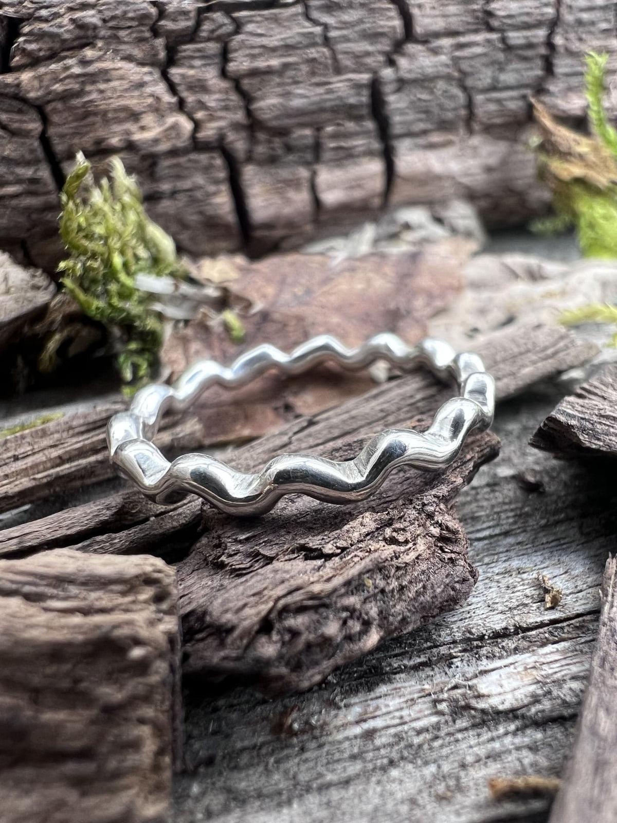 Handmade sterling silver wave ring on weathered driftwood, overhead view showing the full wave band from above