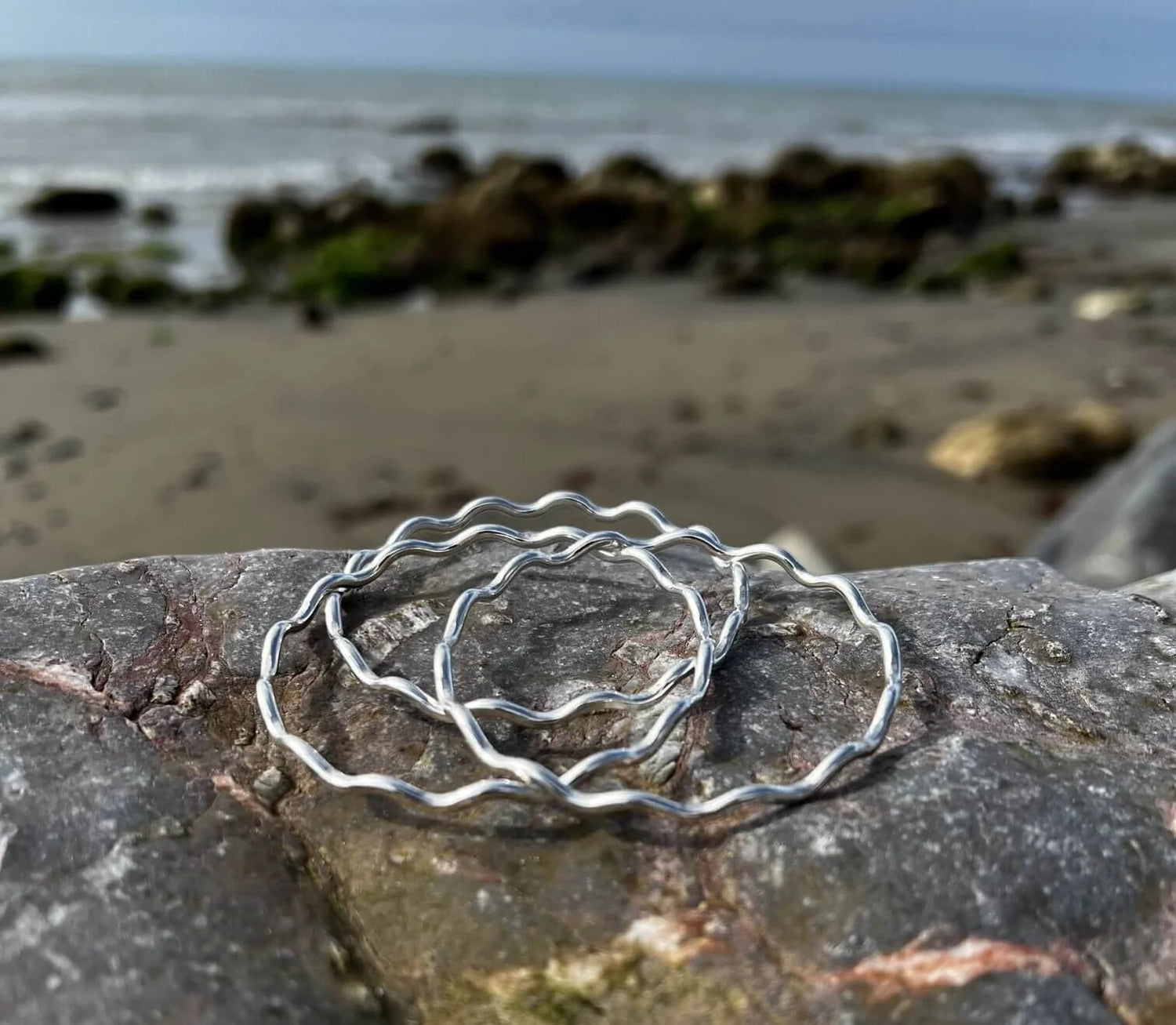 Three Wave Bangles Displayed on a Rock on the Beach - Kerry Gallop Jewellery
