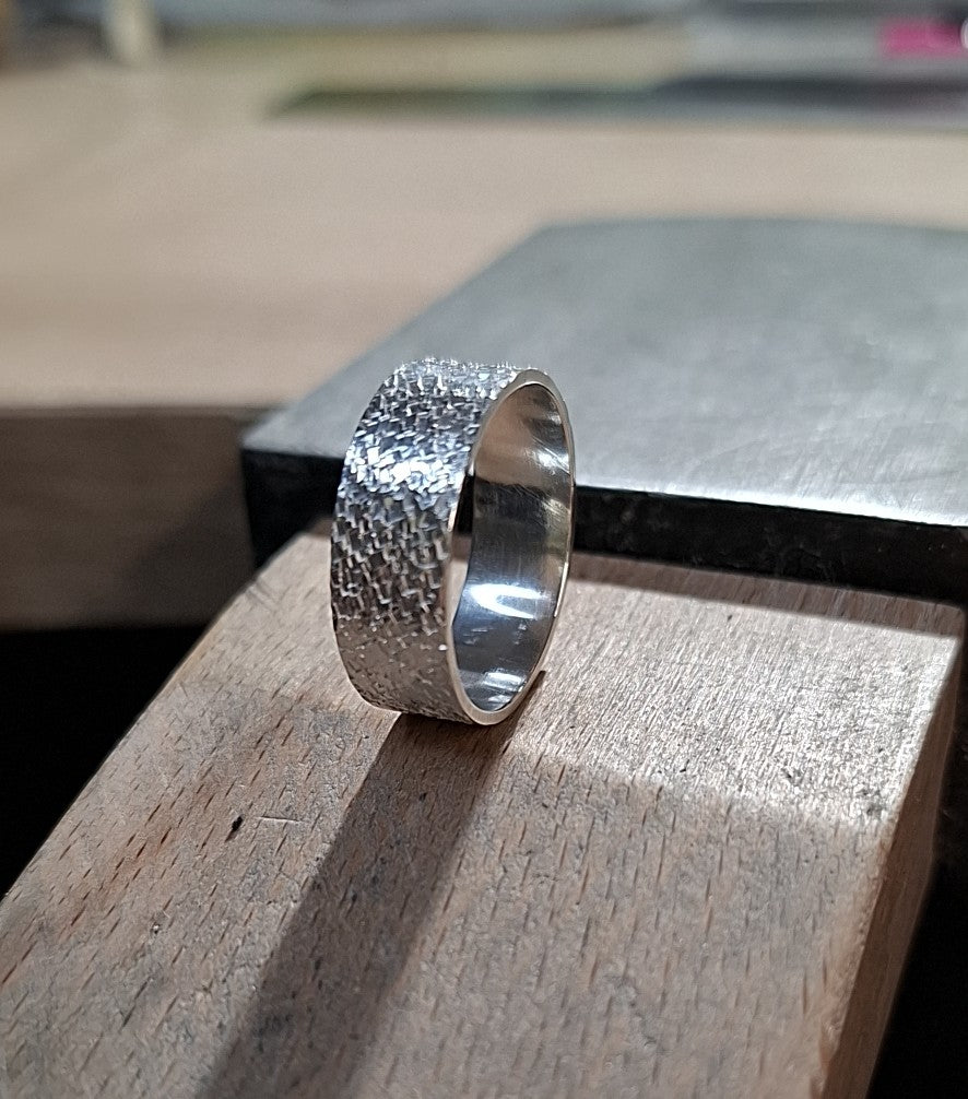 Silver ring with textured design on a wooden surface
