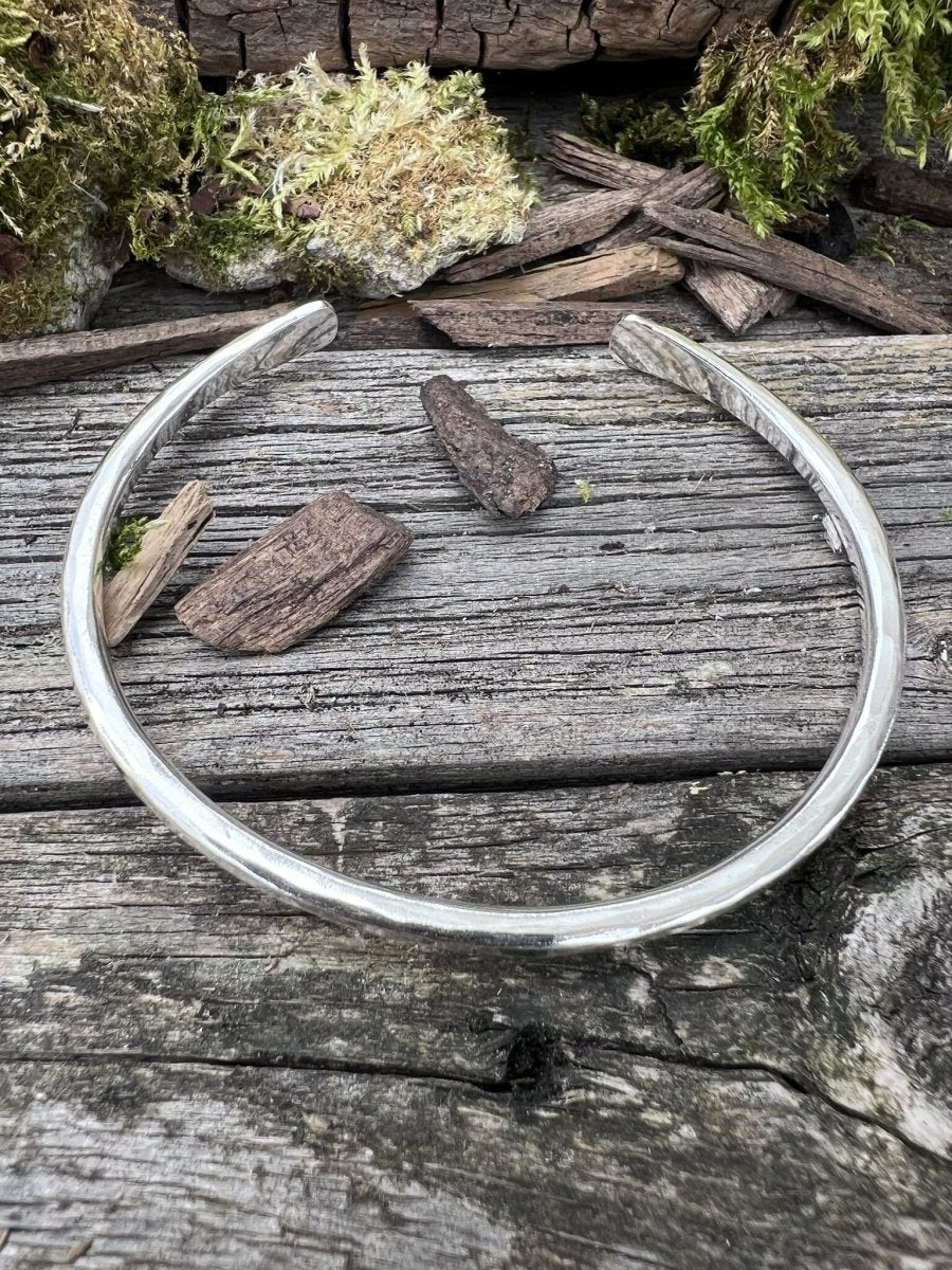 Handmade sterling silver 3.5mm Aurora Crescent torque bangle on weathered wood with bark and moss, side angle view