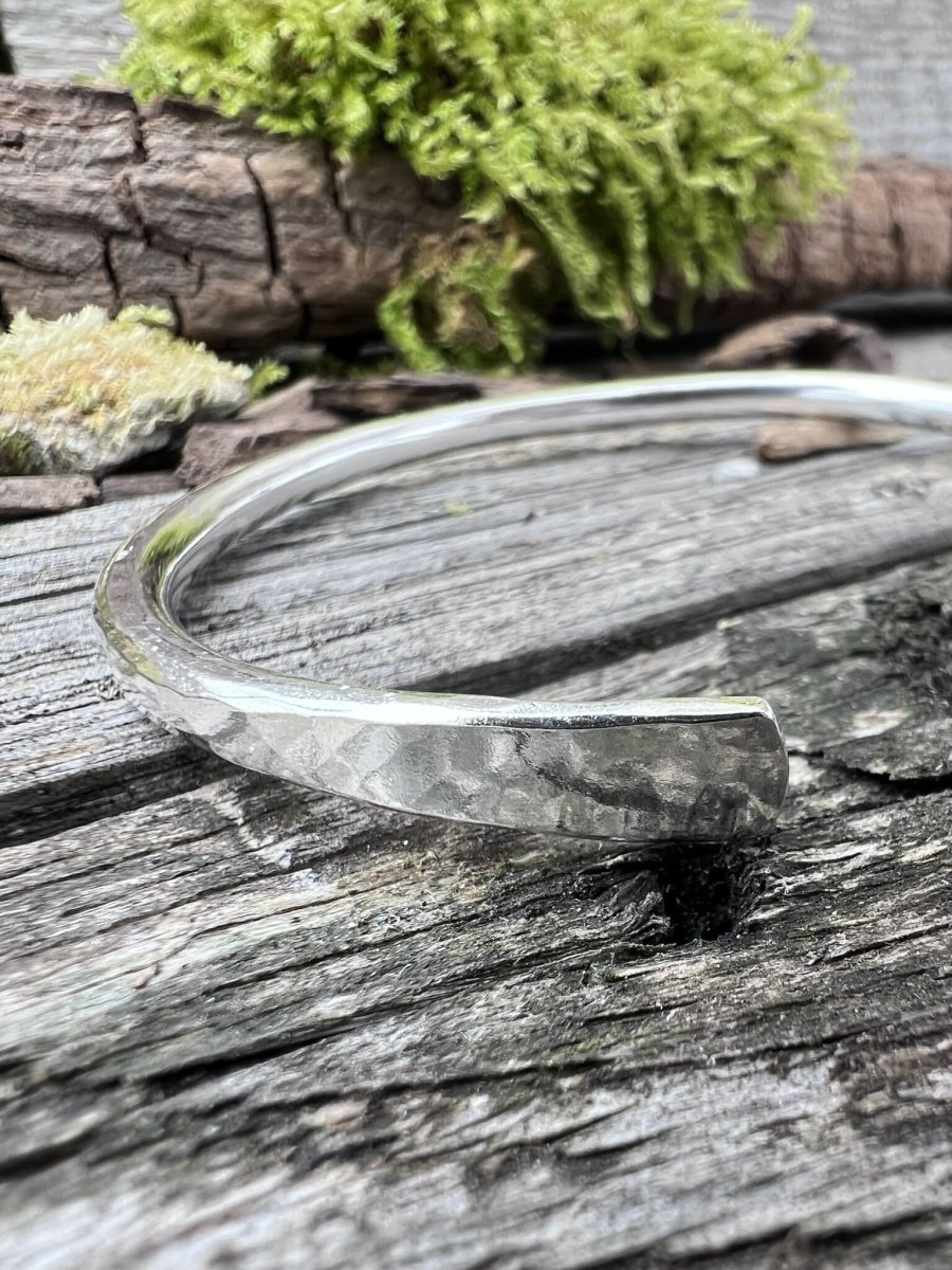 Handmade sterling silver Aurora Crescent torque bangle on weathered wood with moss, photographed from a side angle
