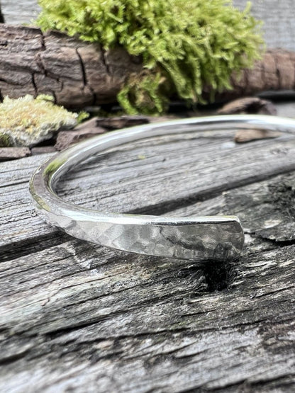 Handmade sterling silver Aurora Crescent torque bangle on weathered wood with moss, photographed from a side angle
