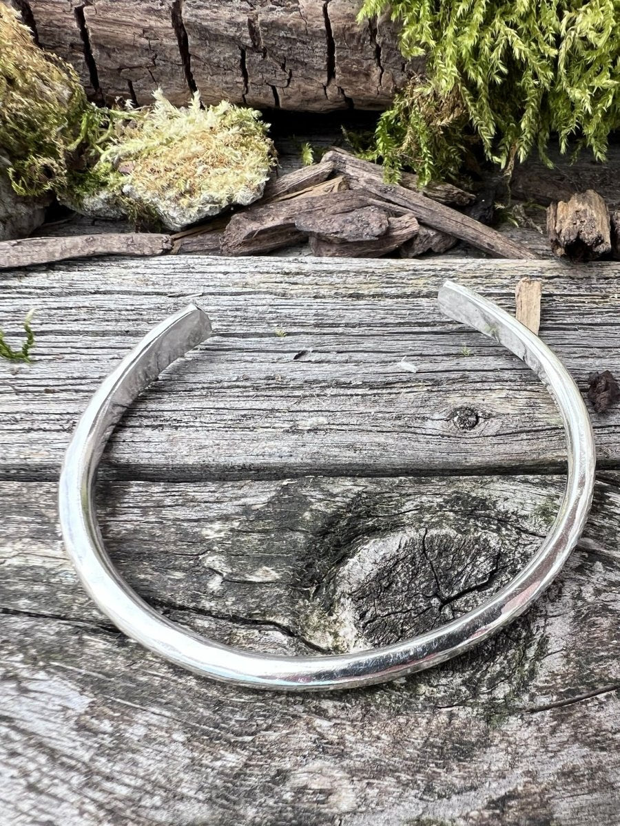 Recycled sterling silver Aurora Crescent torque bangle, 4mm, resting on weathered wood with green moss