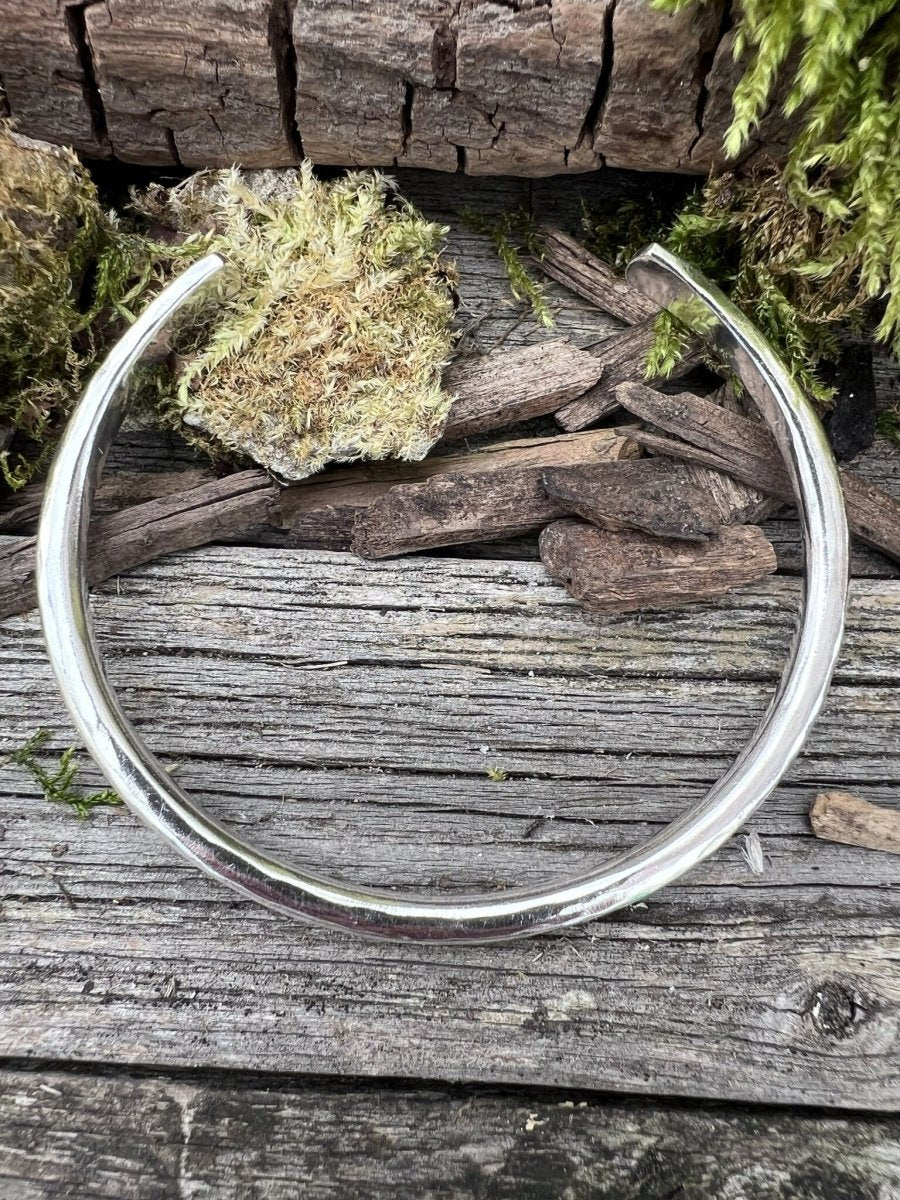 Recycled sterling silver 4mm Aurora Crescent torque bangle styled in a circular open position on mossy weathered wood