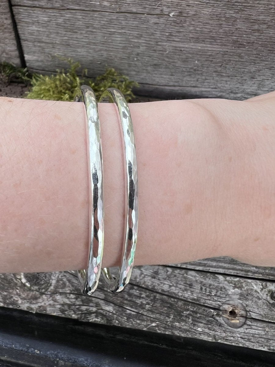 Two recycled sterling silver Aurora Crescent torque bangles stacked together on a wrist, showing how they layer