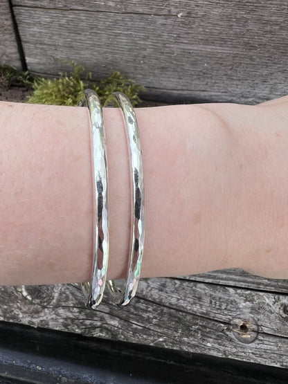 Two recycled sterling silver Aurora Crescent torque bangles stacked together on a wrist, showing how they layer