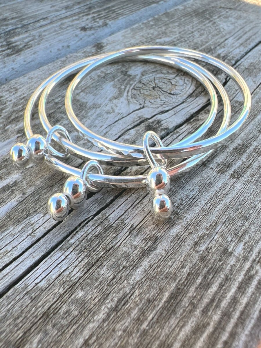 Recycled sterling silver bauble charm bangles styled together on weathered wood, handmade Isle of Wight jewellery