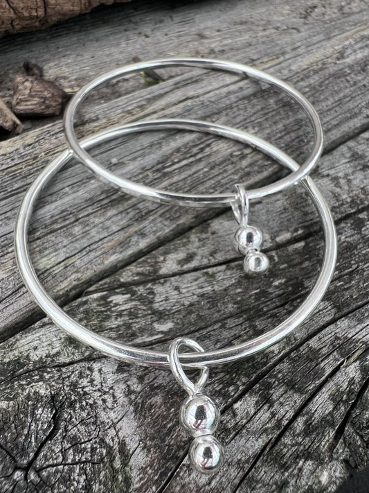 Recycled sterling silver bauble charm bangle on weathered wood, showing the fine wire band and dangling bead charms