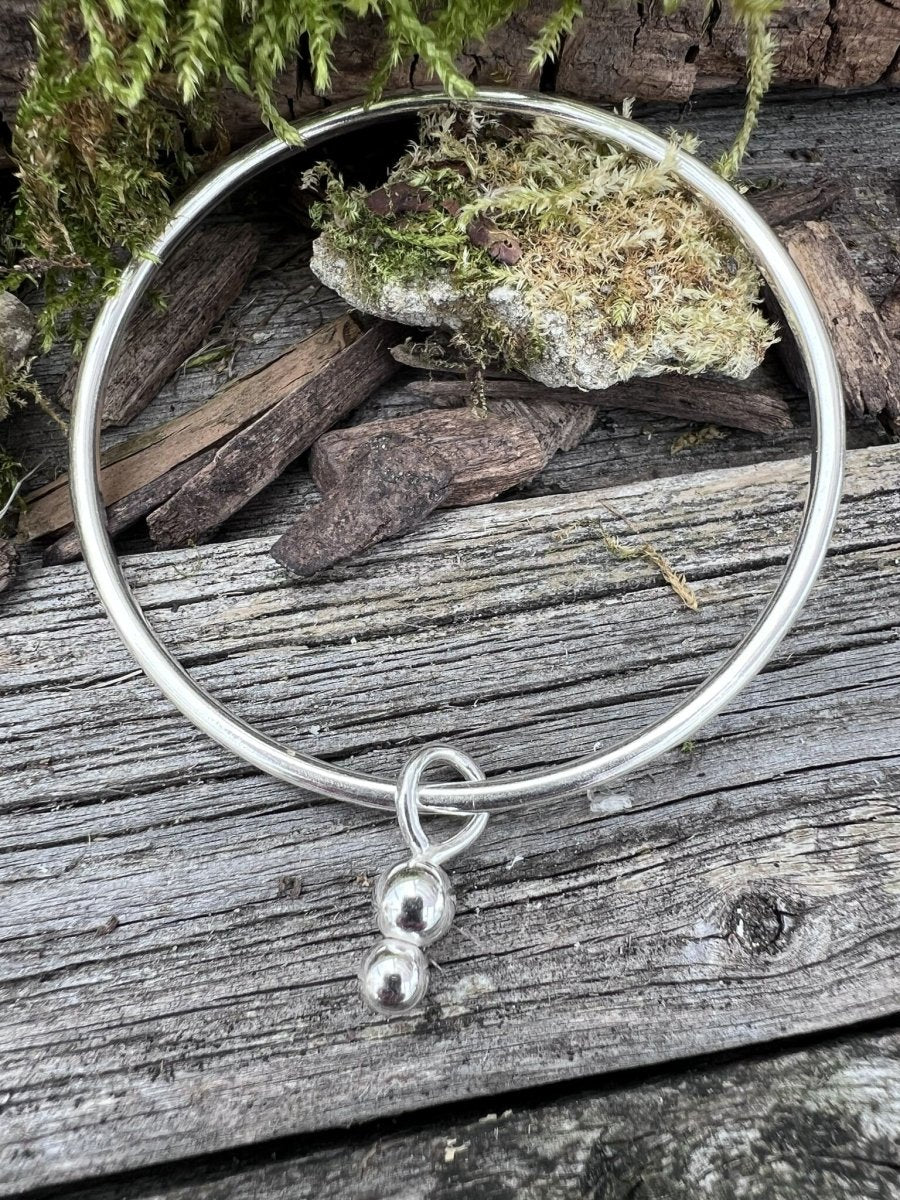 Recycled sterling silver bauble charm bangle styled on mossy wood, showing the full circular band with charms