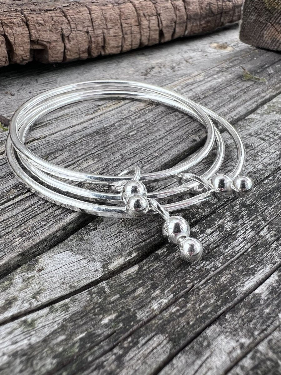 Handmade sterling silver bauble charm bangles photographed from above on wood, showing the bead charm detail