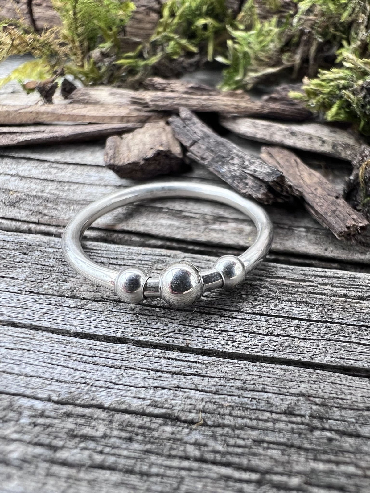 Handmade sterling silver beaded spinner ring on driftwood, front angle showing the spinning bead band profile