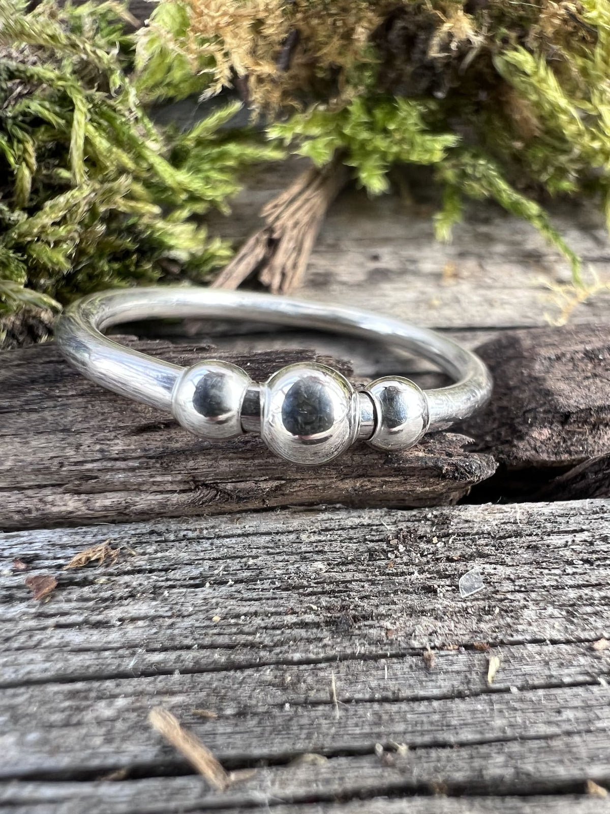 Close-up of a handmade sterling silver beaded spinner ring on moss, highlighting the spinning beaded outer band detail