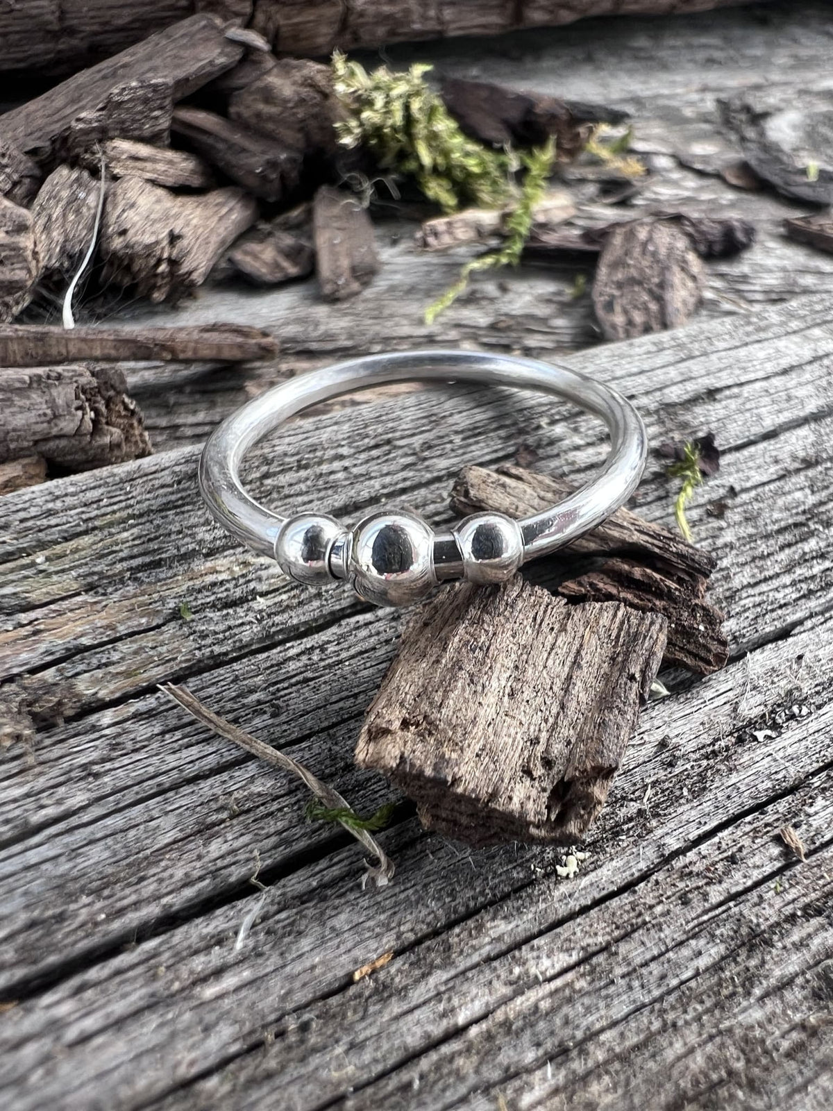 Recycled sterling silver beaded spinner ring on weathered driftwood, showing the plain band with spinning beaded outer ring
