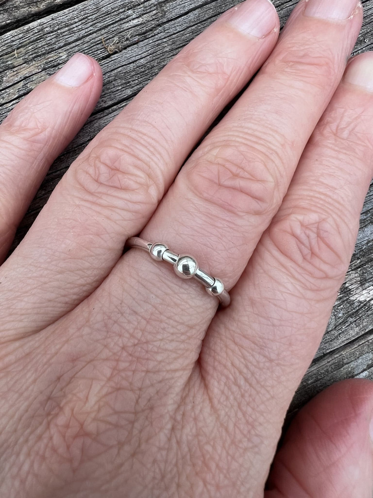Sterling silver beaded spinner ring worn on a finger, showing the delicate spinning bead band and scale