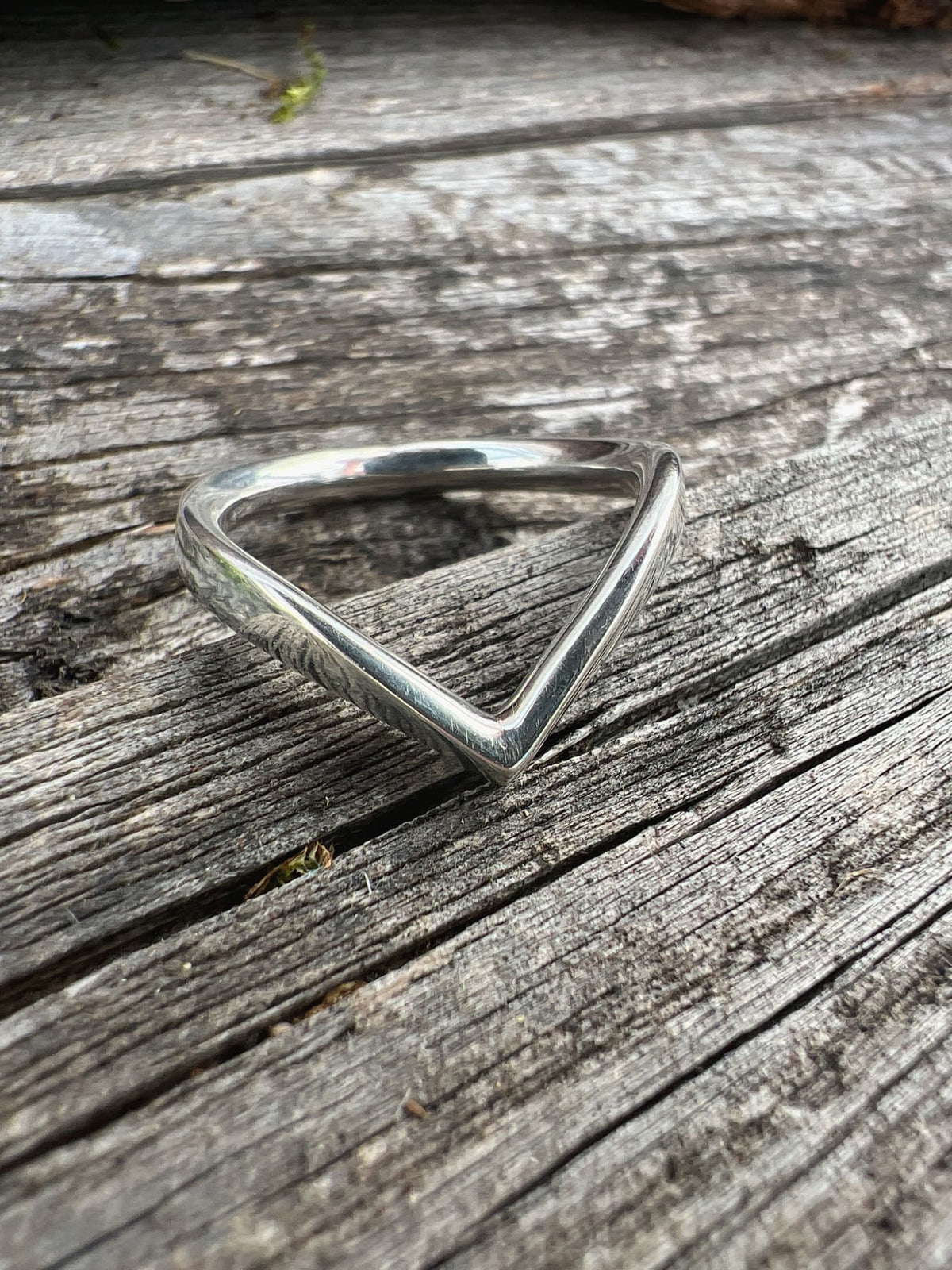 Handmade sterling silver chevron ring on driftwood, side angle showing the pointed V-band profile