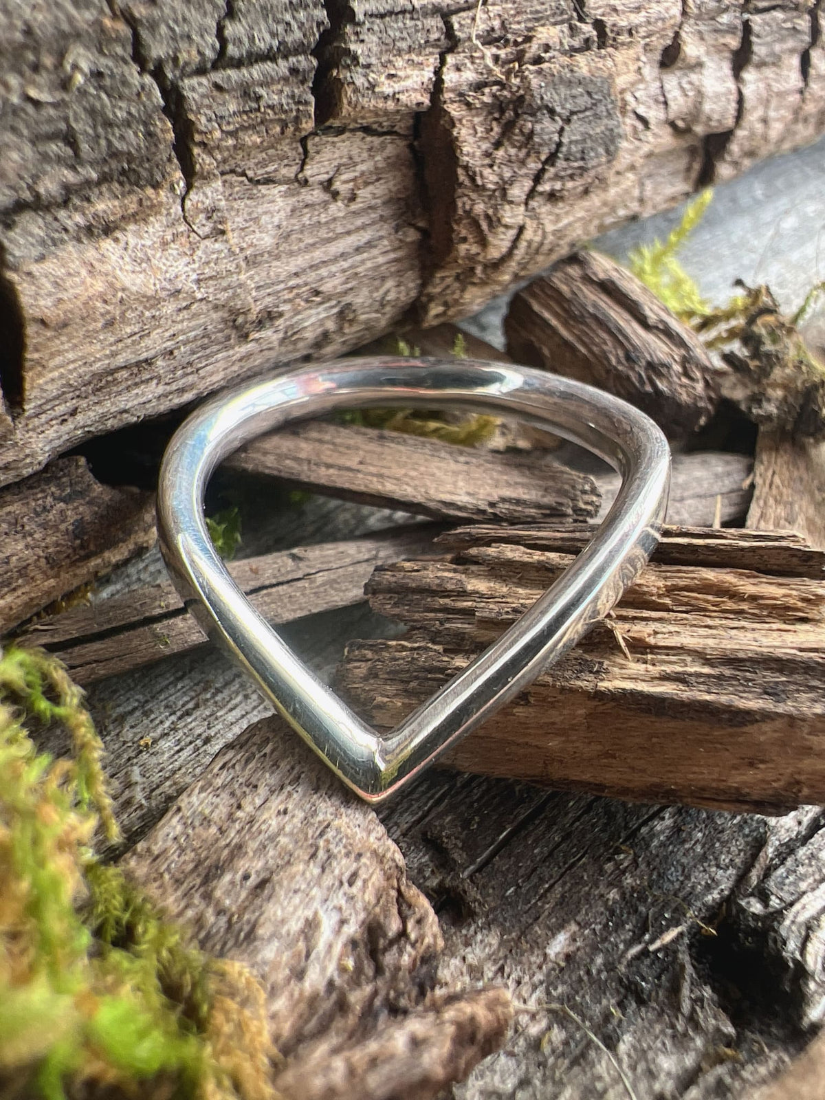 Handmade sterling silver chevron ring on mossy driftwood, showing the geometric V-shape from an angled view