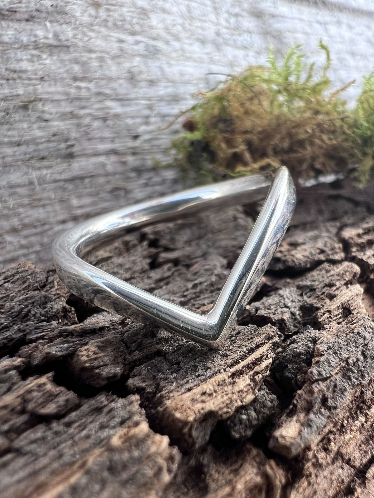 Close-up of a handmade sterling silver chevron ring on driftwood, highlighting the pointed V-shape and polished finish