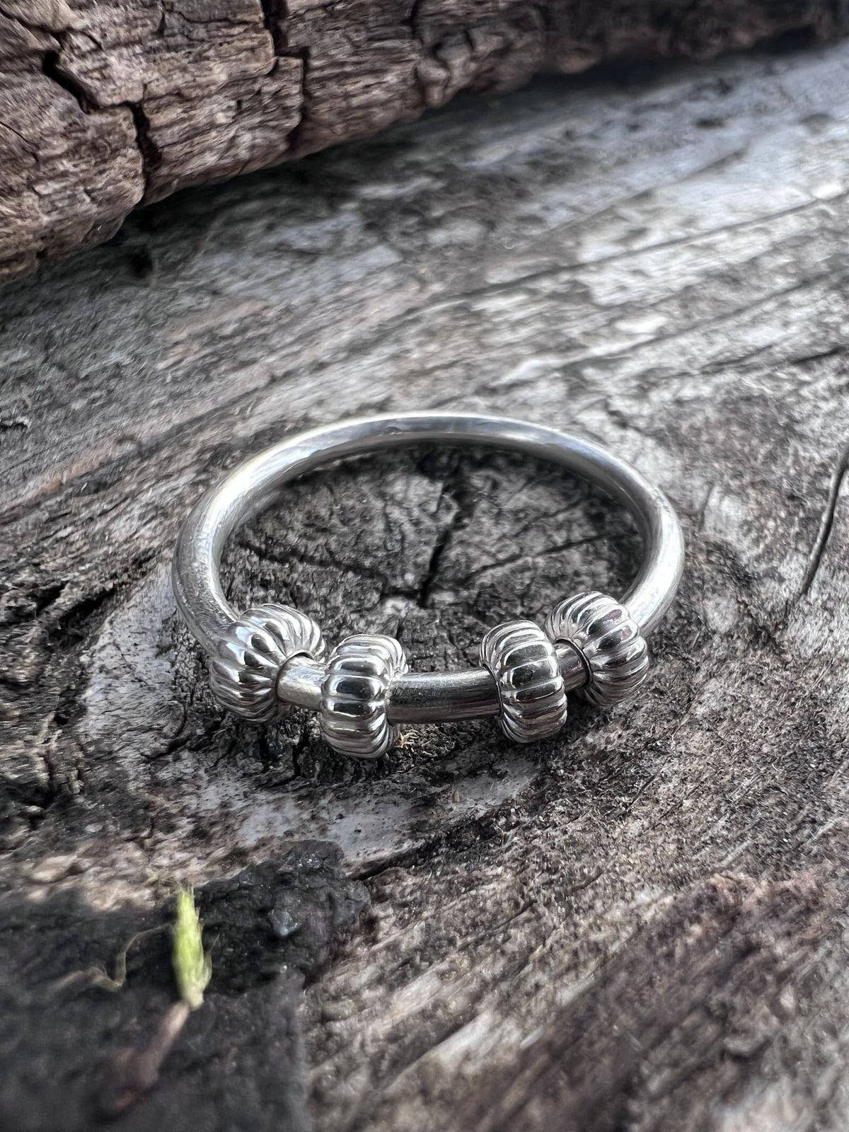 Handmade sterling silver corrugated spinner ring on driftwood, side angle showing the ridged bead profile