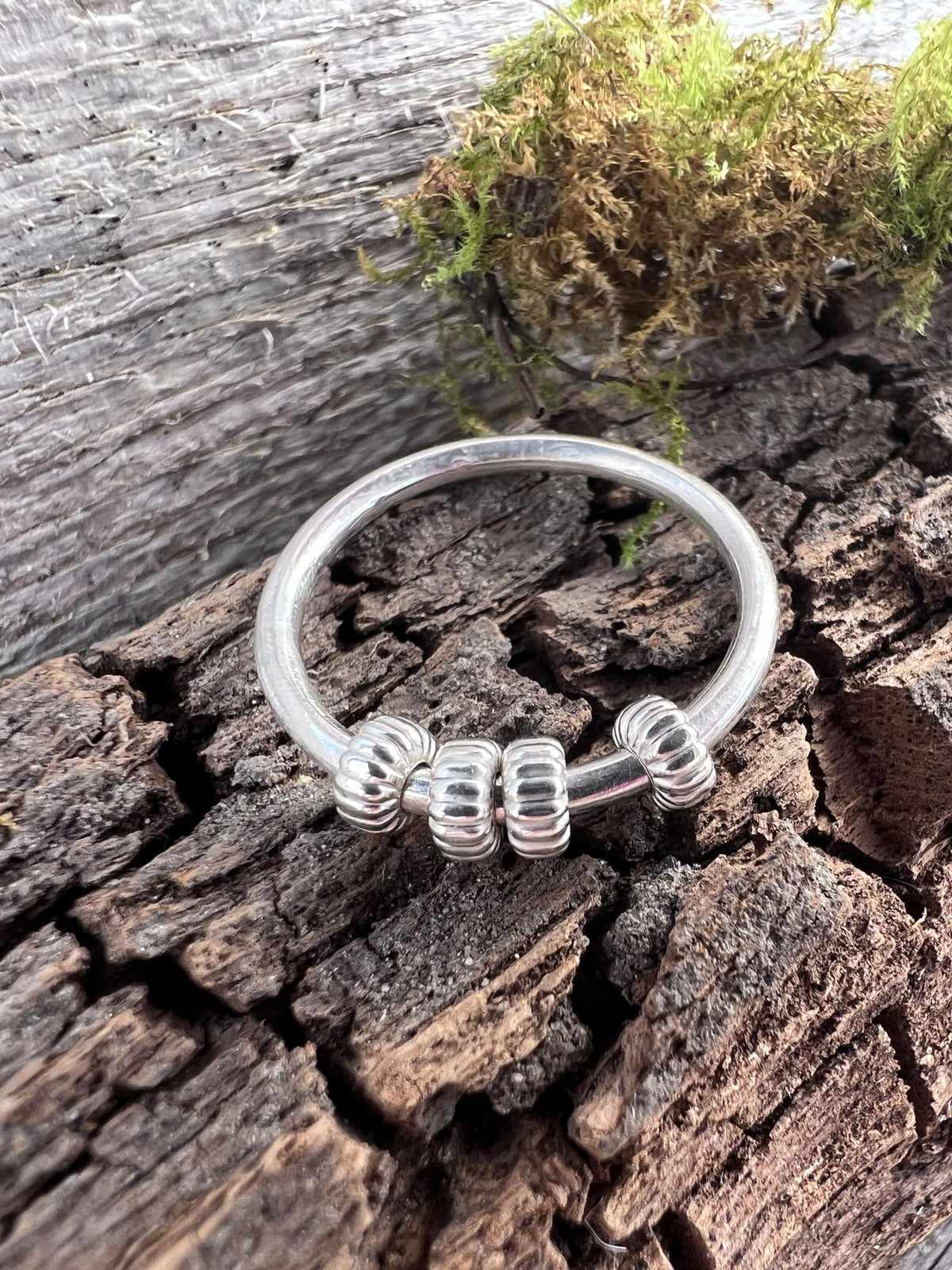 Recycled sterling silver corrugated spinner ring on mossy driftwood, showing the ridged spinning bead detail
