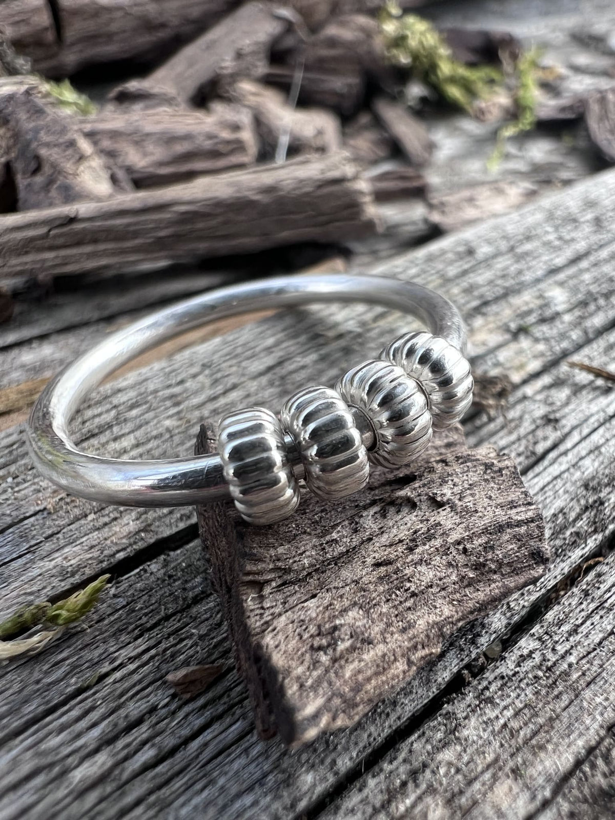 Recycled sterling silver corrugated spinner ring on driftwood, showing the ridged spinning outer beads on a plain inner band
