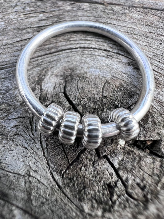 Close-up of a handmade sterling silver corrugated spinner ring, showing the ridged texture on the spinning outer beads