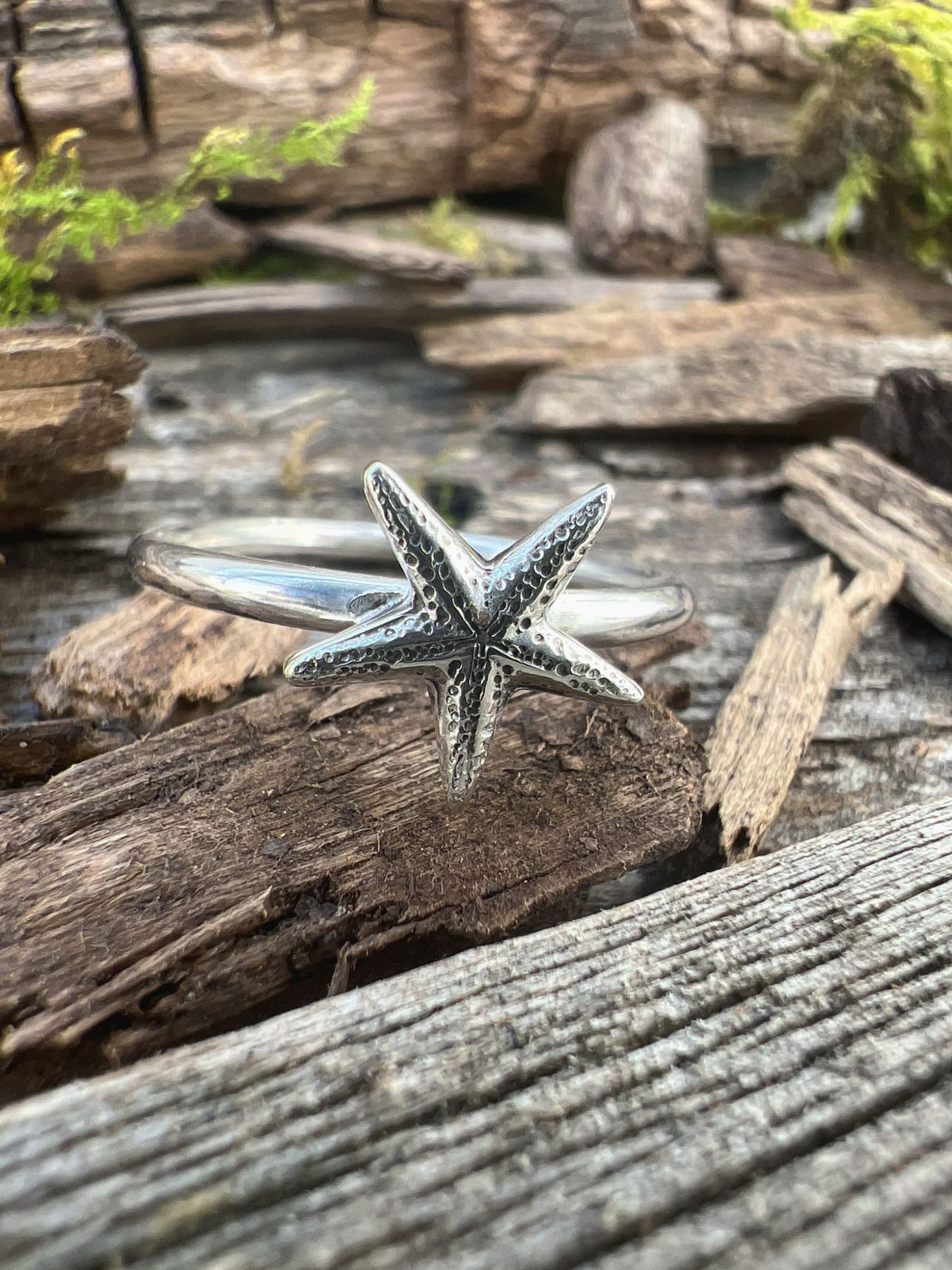 Recycled sterling silver delicate starfish ring on driftwood, showing the fine starfish from a slightly angled view