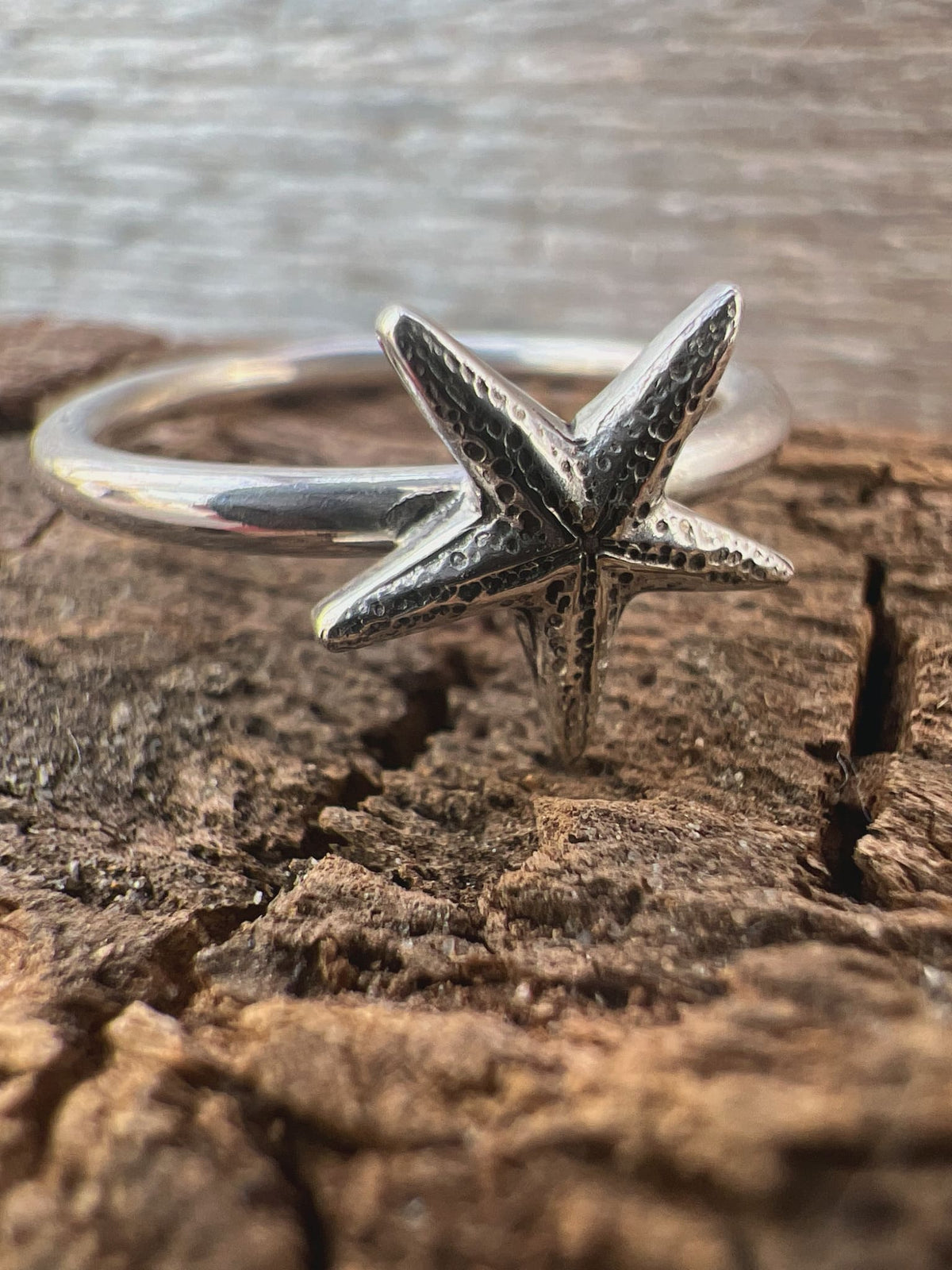 Close-up of a handmade sterling silver delicate starfish ring on driftwood, showing the fine pointed starfish detail