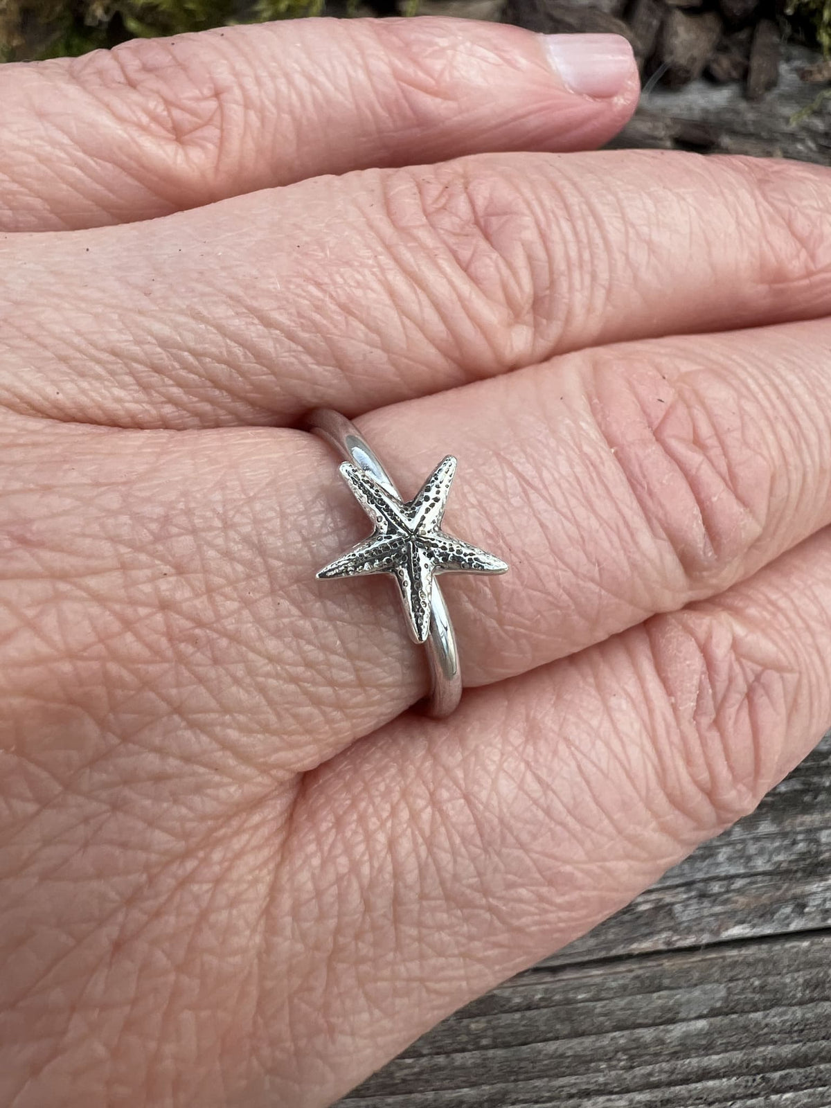 Sterling silver delicate starfish ring worn on a finger, showing the dainty scale of the starfish on the slim band