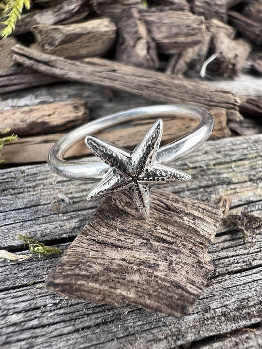 Recycled sterling silver delicate starfish ring on weathered driftwood, showing the fine starfish motif on a slim band