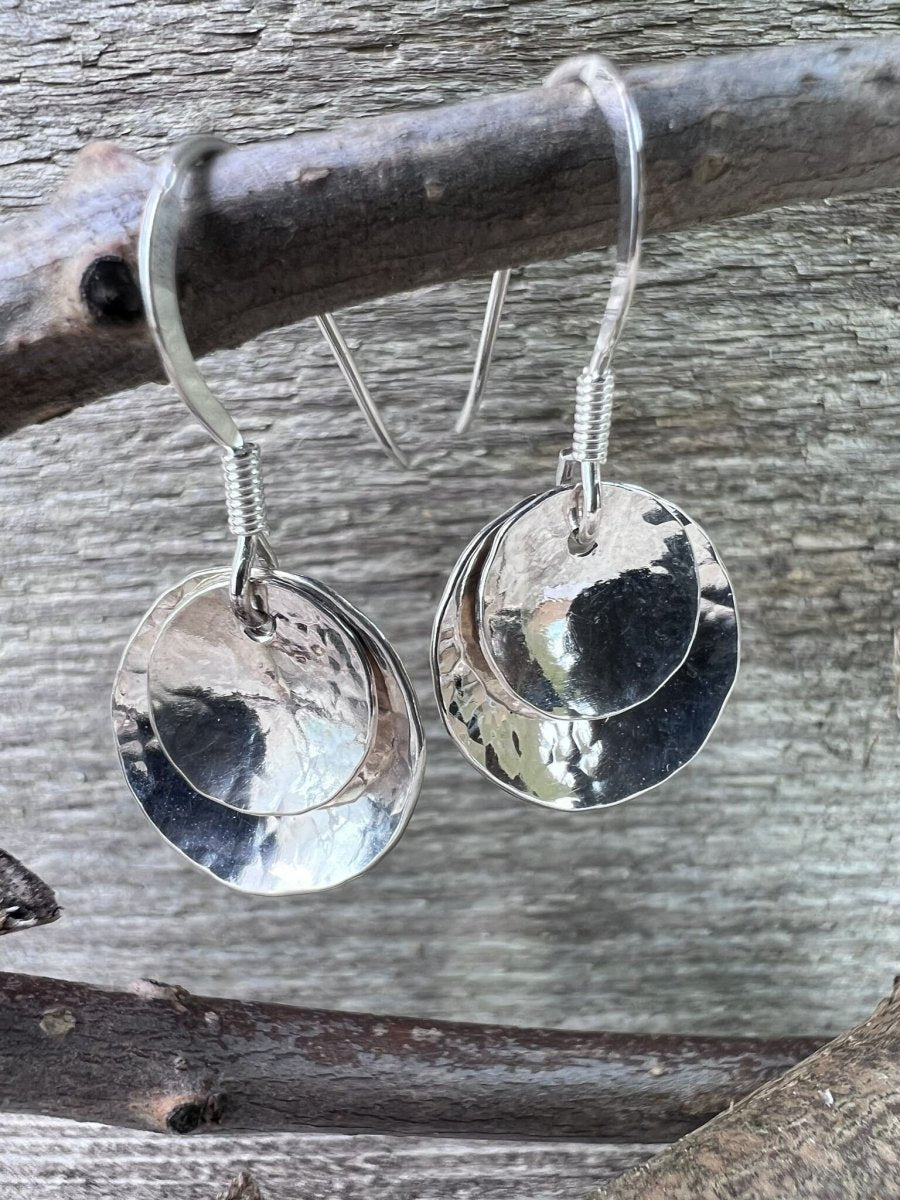 Handmade sterling silver double domed earrings photographed from a low angle on wooden branch, showing the dome profile