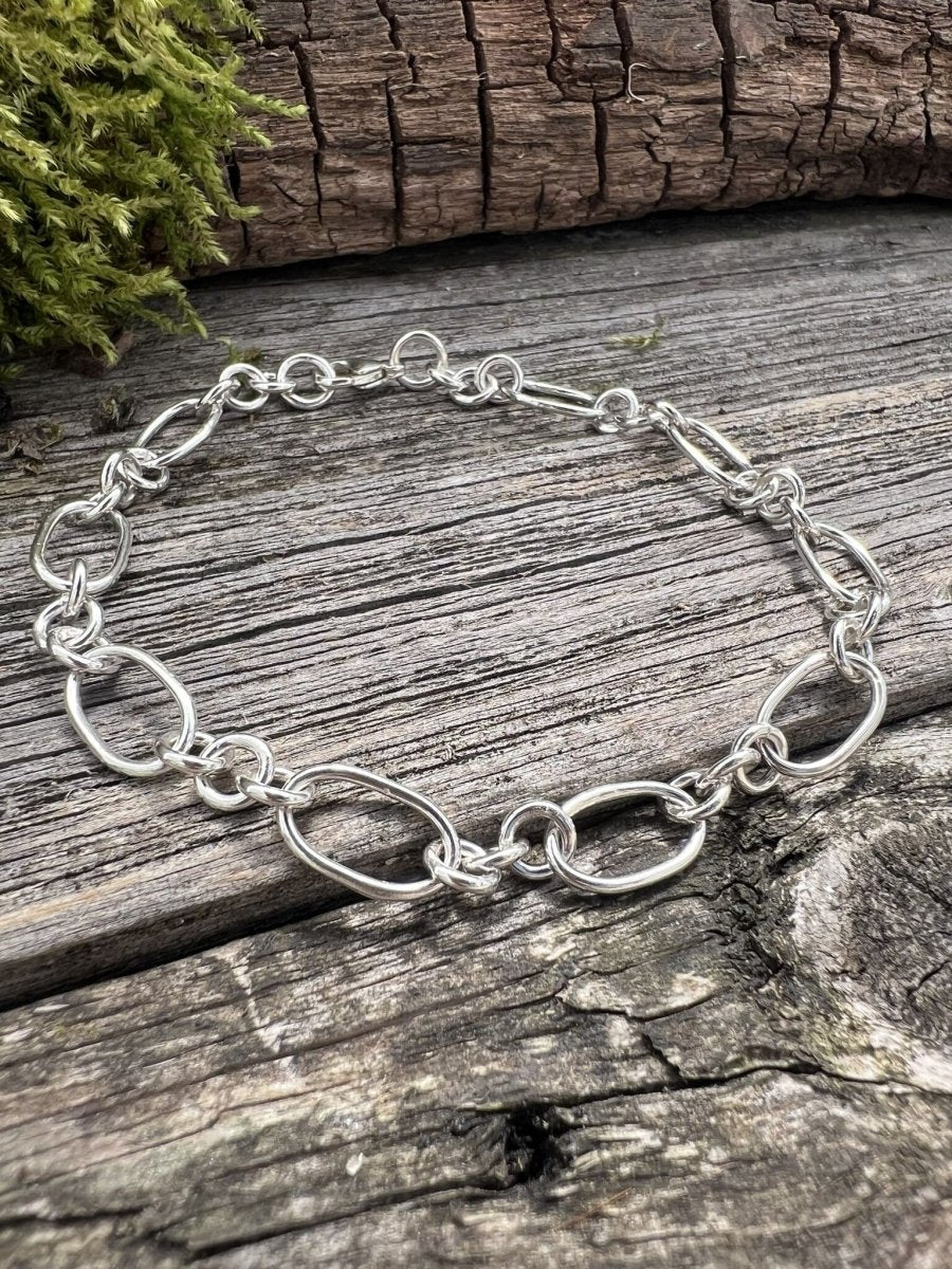Handmade sterling silver fetter and three link bracelet on mossy weathered wood, side angle showing the chain structure