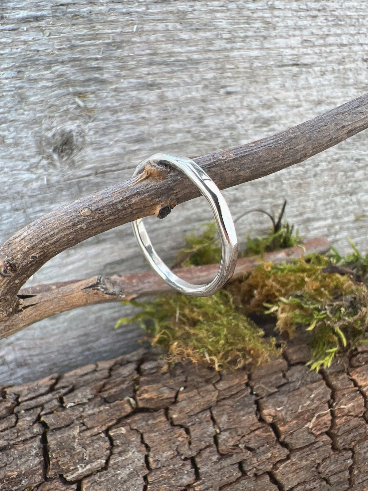 Handmade sterling silver flat hammered ring on driftwood with moss, showing the open band ends and flat profile