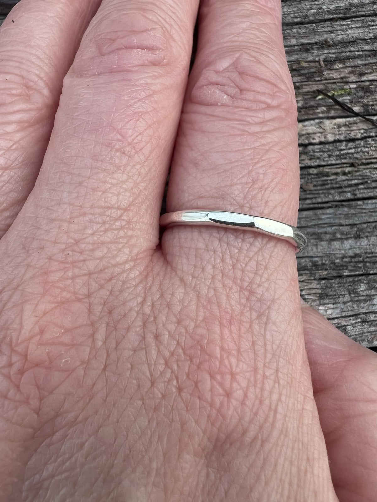 Sterling silver flat hammered ring worn on a finger, showing scale and the thin flat band
