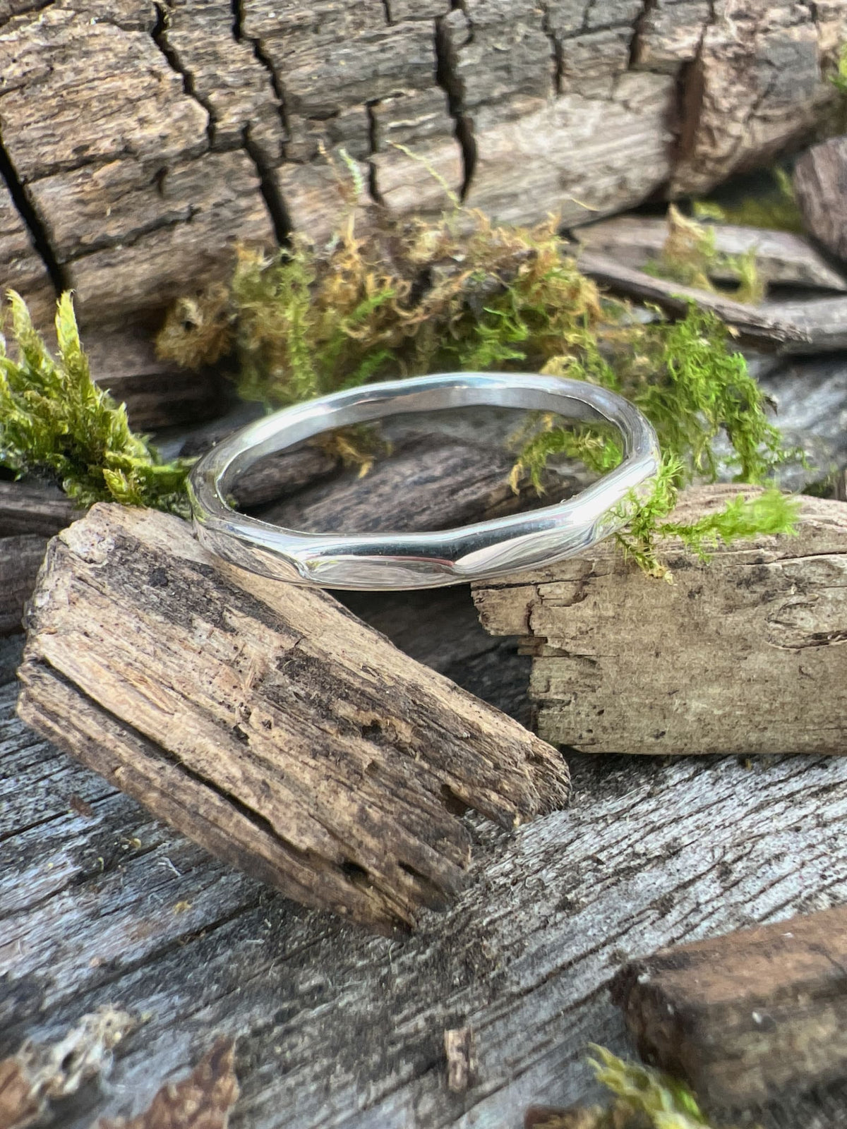 Handmade sterling silver flat hammered ring on driftwood, side angle showing the flat thin band width