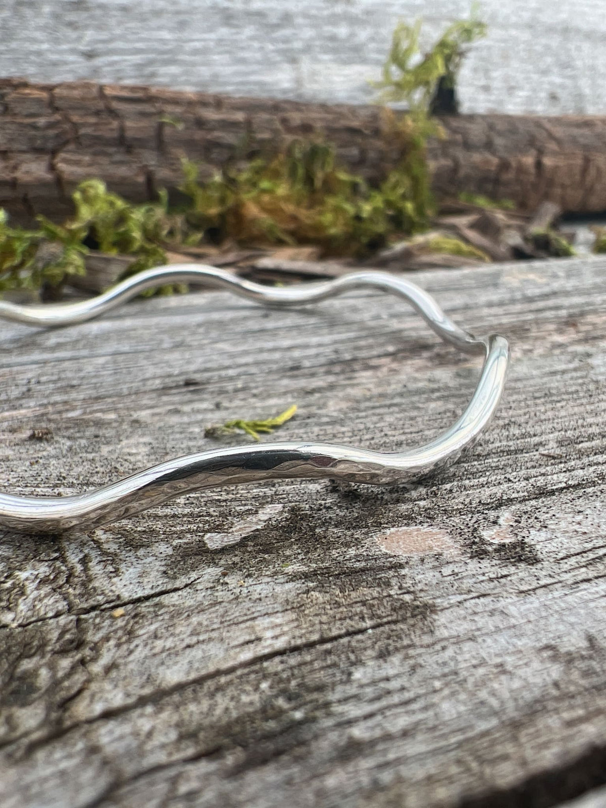 Close-up of a handmade sterling silver gentle wave bangle 2.5mm on driftwood, showing the gentle curves and hammered texture