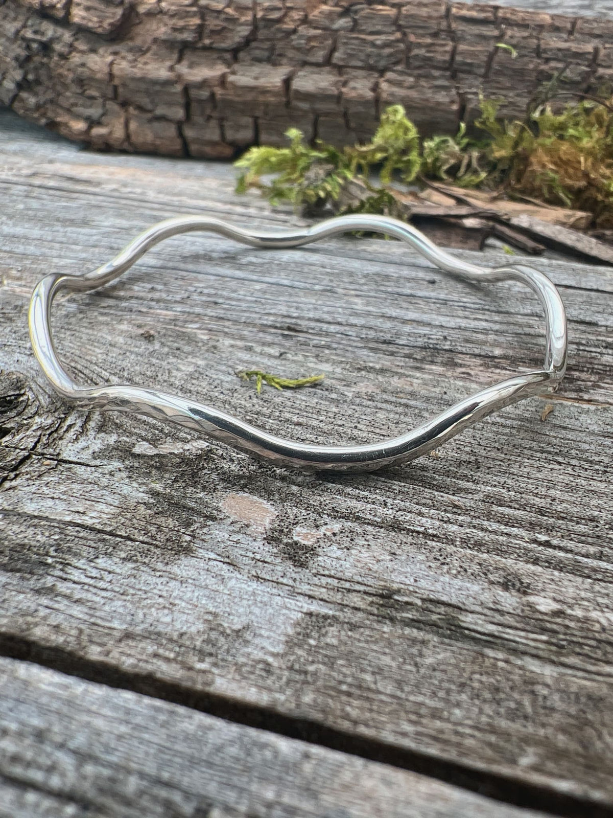 Recycled sterling silver gentle wave bangle 2.5mm on weathered driftwood, showing the smooth undulating wave form