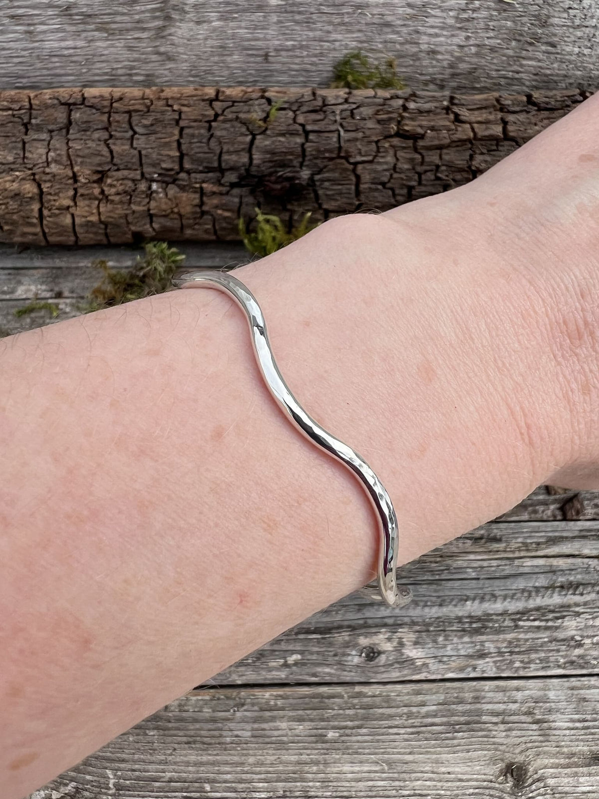 Sterling silver gentle wave bangle 2.5mm worn on a wrist, showing scale and the subtle flowing wave shape