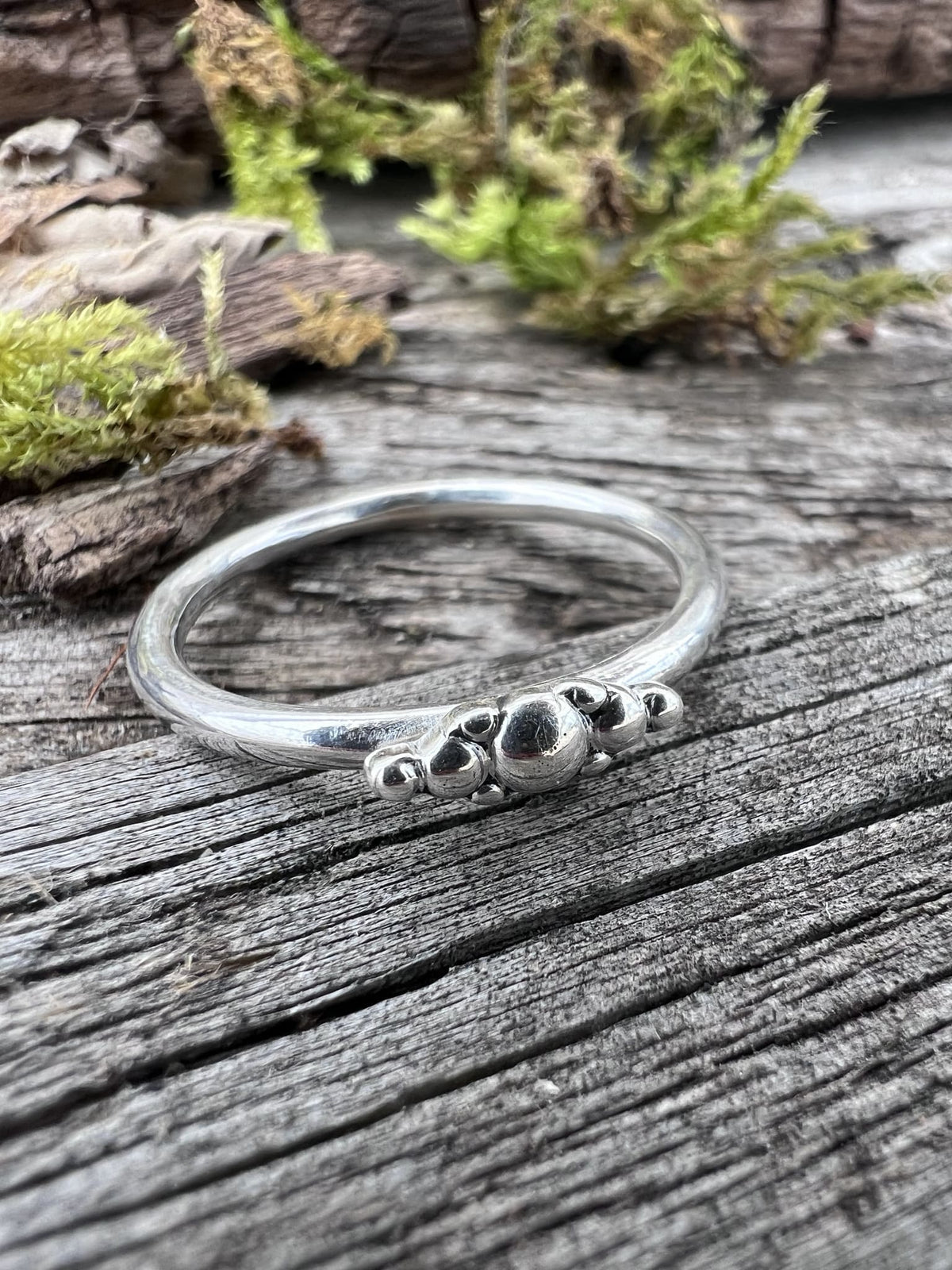 Handmade sterling silver granule row ring on mossy driftwood, angled view showing the row of silver granules